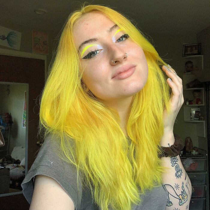 Young woman with vibrant yellow hair, showcasing a new hair color style in a casual room setting.