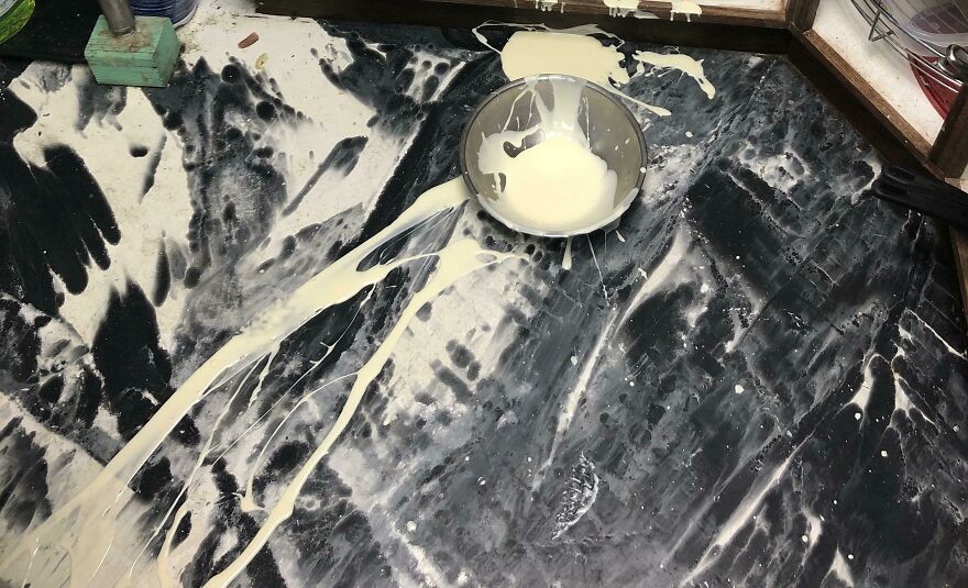 A bowl of spilled cream on a dark marbled surface creates an accidental art pic, resembling an abstract painting.