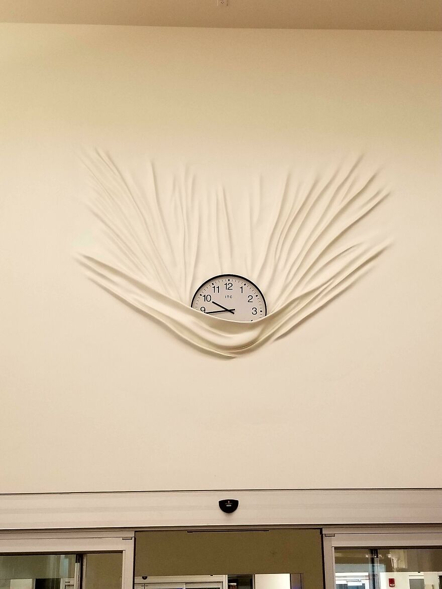 Clock surrounded by wall folds resembling fabric, creating an accidental art effect.