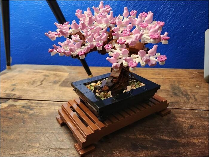 Toy bonsai tree with pink flowers on a wooden table, adding joy to home decor.