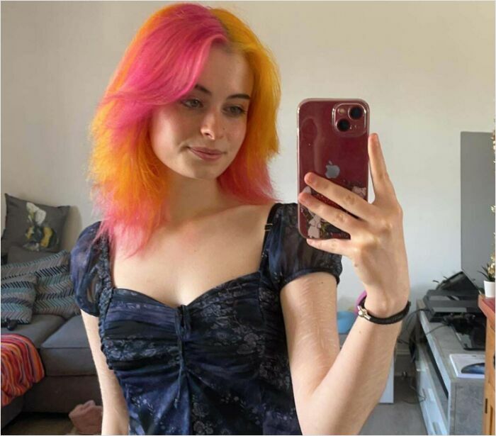 A woman with pink and orange hair takes a selfie, showcasing her new hair color change.