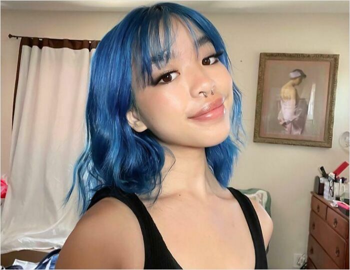 Person with vibrant blue hair smiling in a cozy room, showcasing changing hair color.