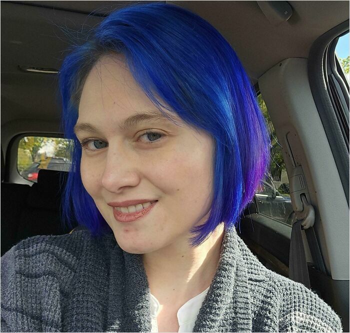 Person with bright blue hair in a car, smiling, showcasing changing hair color.