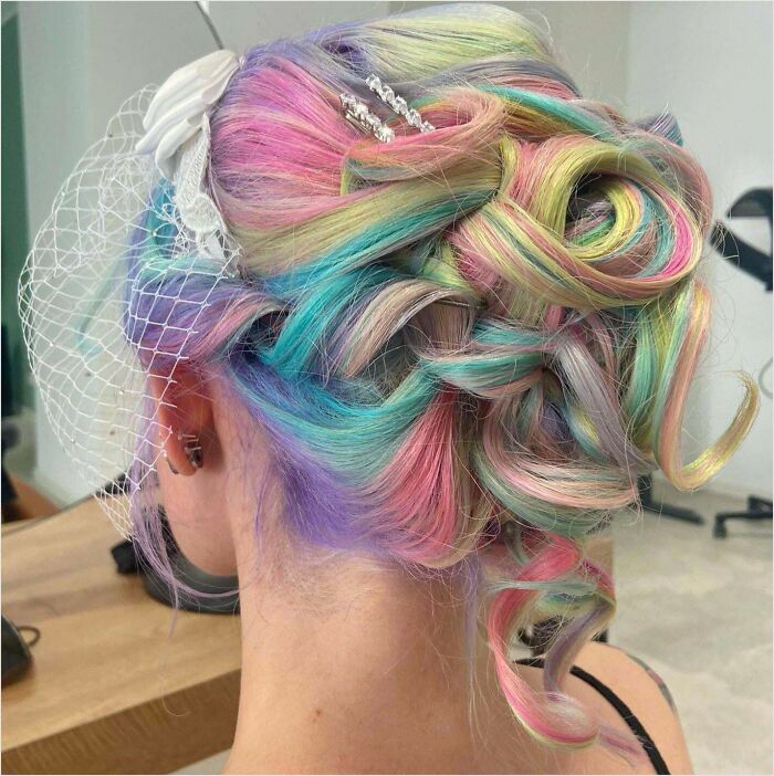 Pastel rainbow updo showcasing creative changing hair color with a white hair accessory and netting.