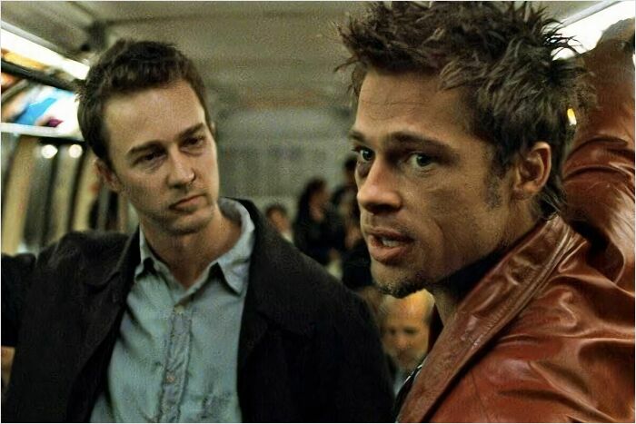 Two men in a subway discussing fascinating fan theories, one in a leather jacket looking determined.