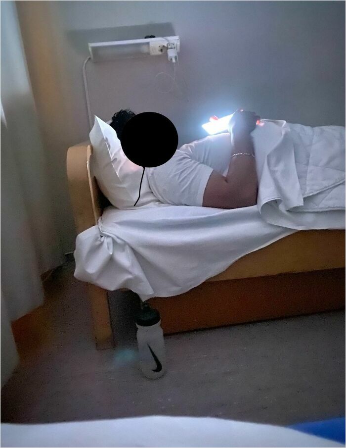 Person in bed using a phone in a dimly lit room, illustrating horrible roommates scenario.