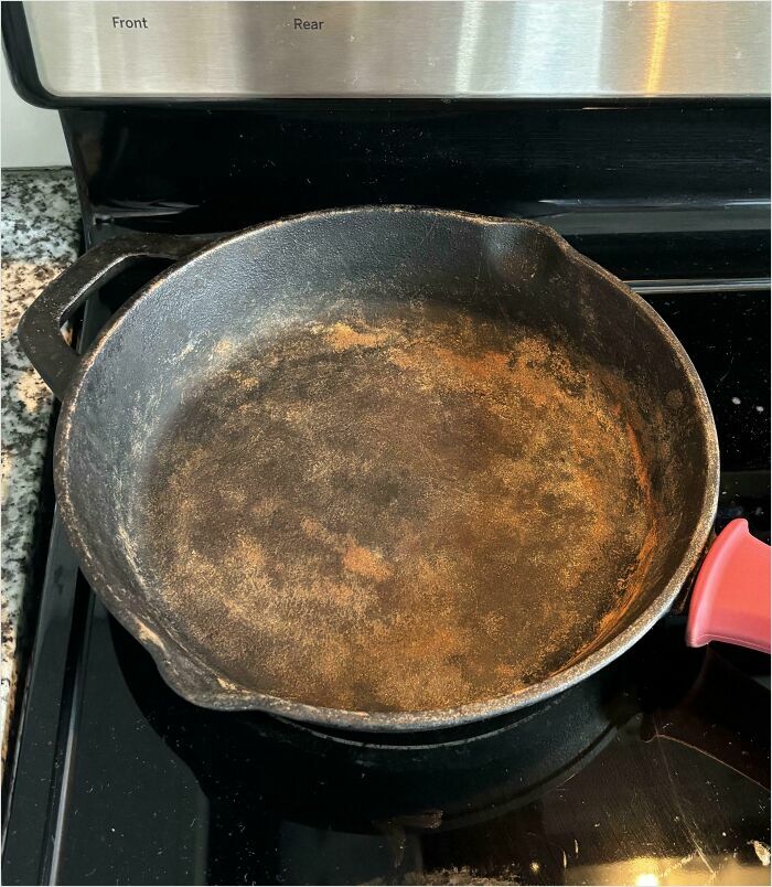 Rusty cast iron skillet left on stove, an example of horrible roommates neglecting cookware care.