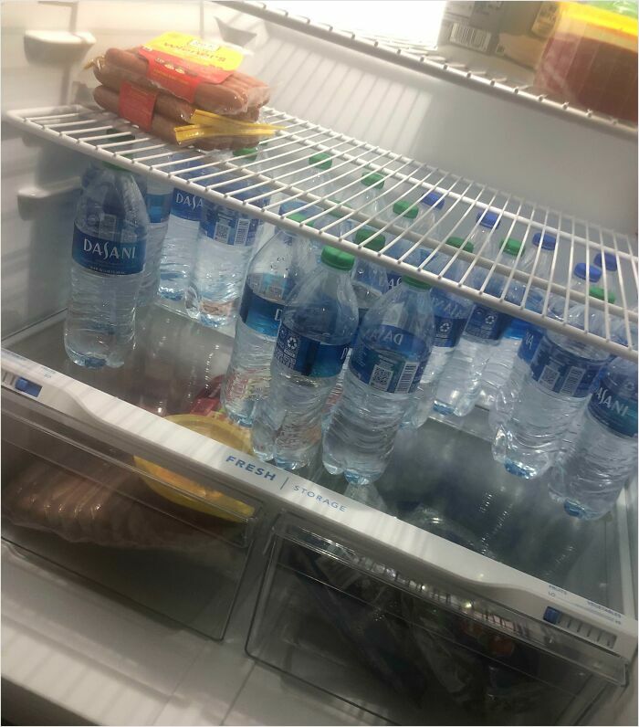 Fridge with water bottles and a pack of hot dogs, showing typical horrible roommates' food storage organization.