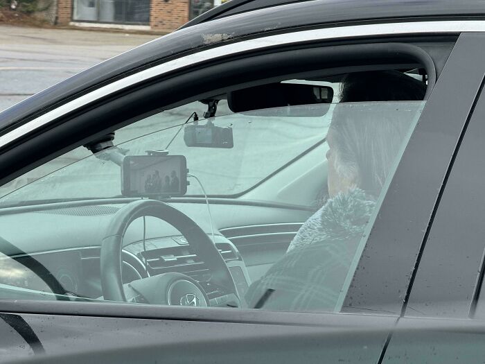 Person distracted by phone on dashboard while driving, exemplifying dangerous behavior for "Idiots-In-Cars" theme.