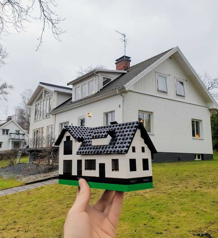 Hand holding a LEGO model house in front of a real house, showcasing cool LEGO builds.