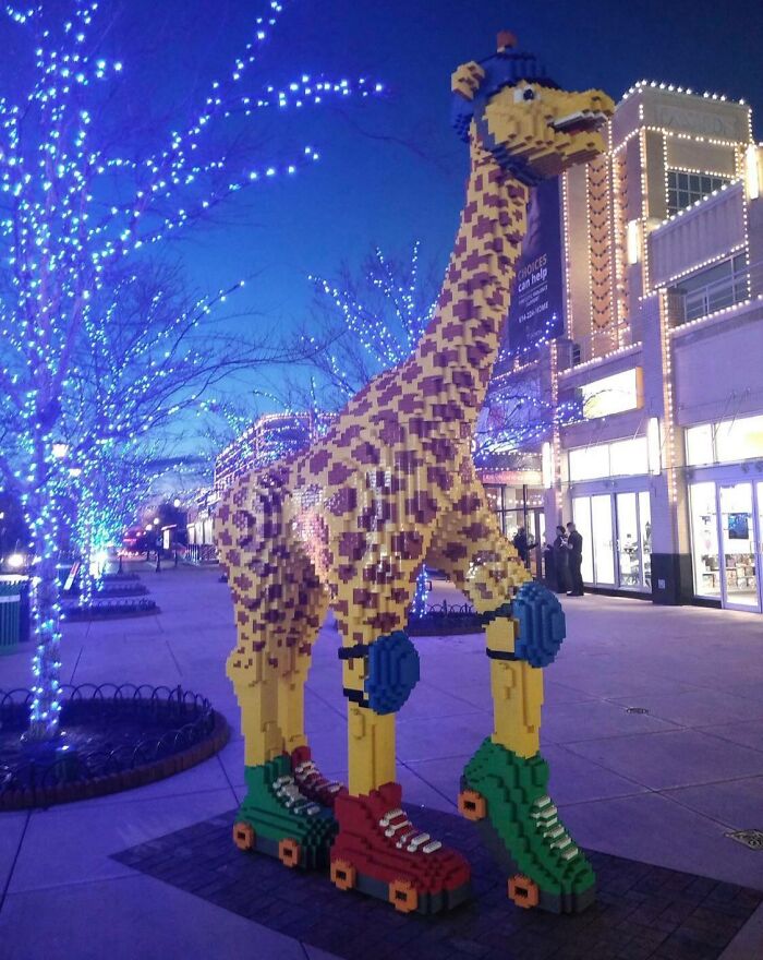 LEGO giraffe build with roller skates, displayed under vibrant blue lights on a city street.