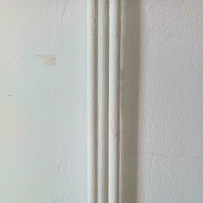 Confusing perspective of a white wall with vertical pipes that blend in, creating an optical illusion.