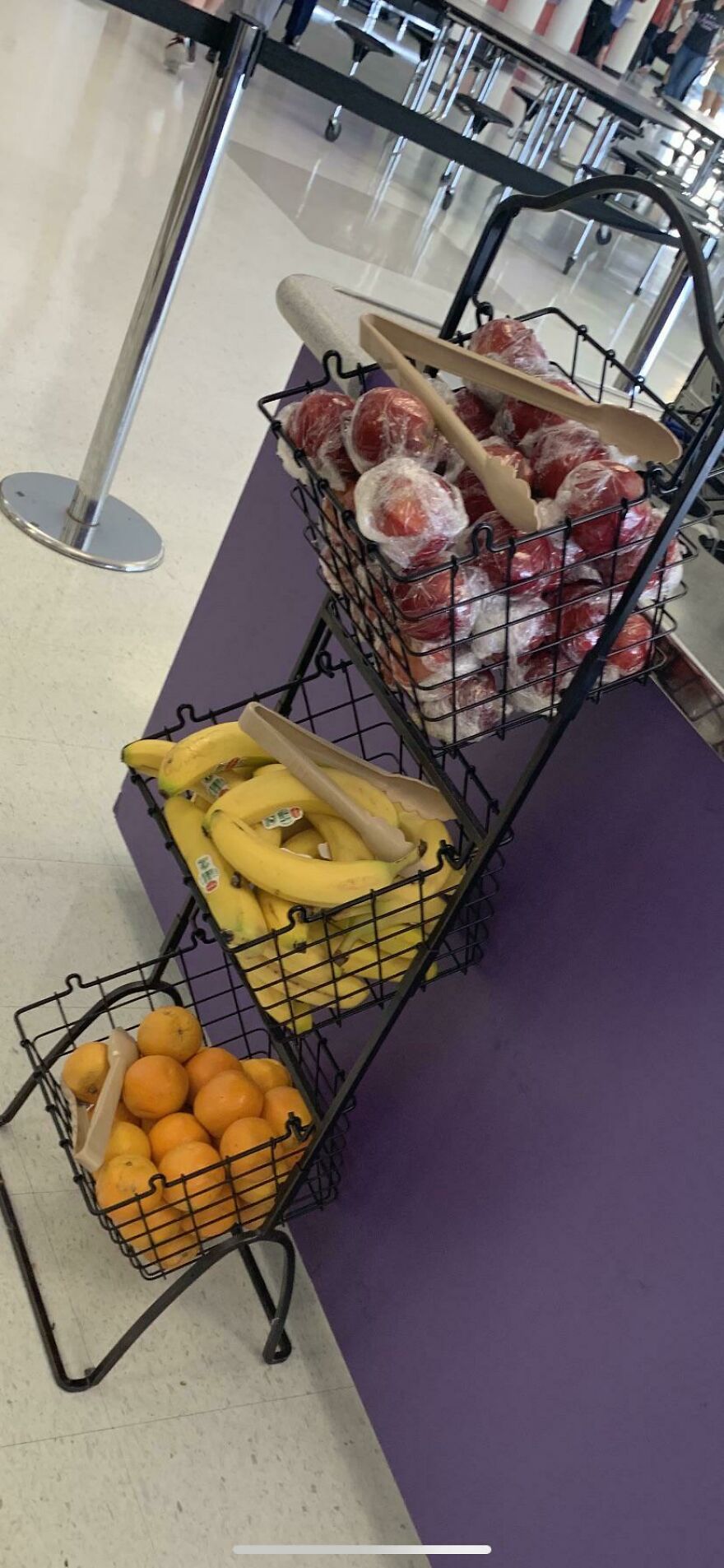 Fruit display with bananas, oranges, and apples wrapped in plastic, highlighting unnecessary packaging in grocery stores.