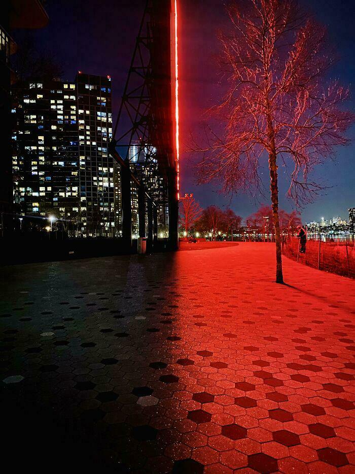 Confusing perspectives image with contrasting red and dark sidewalk, creating an optical illusion against cityscape.