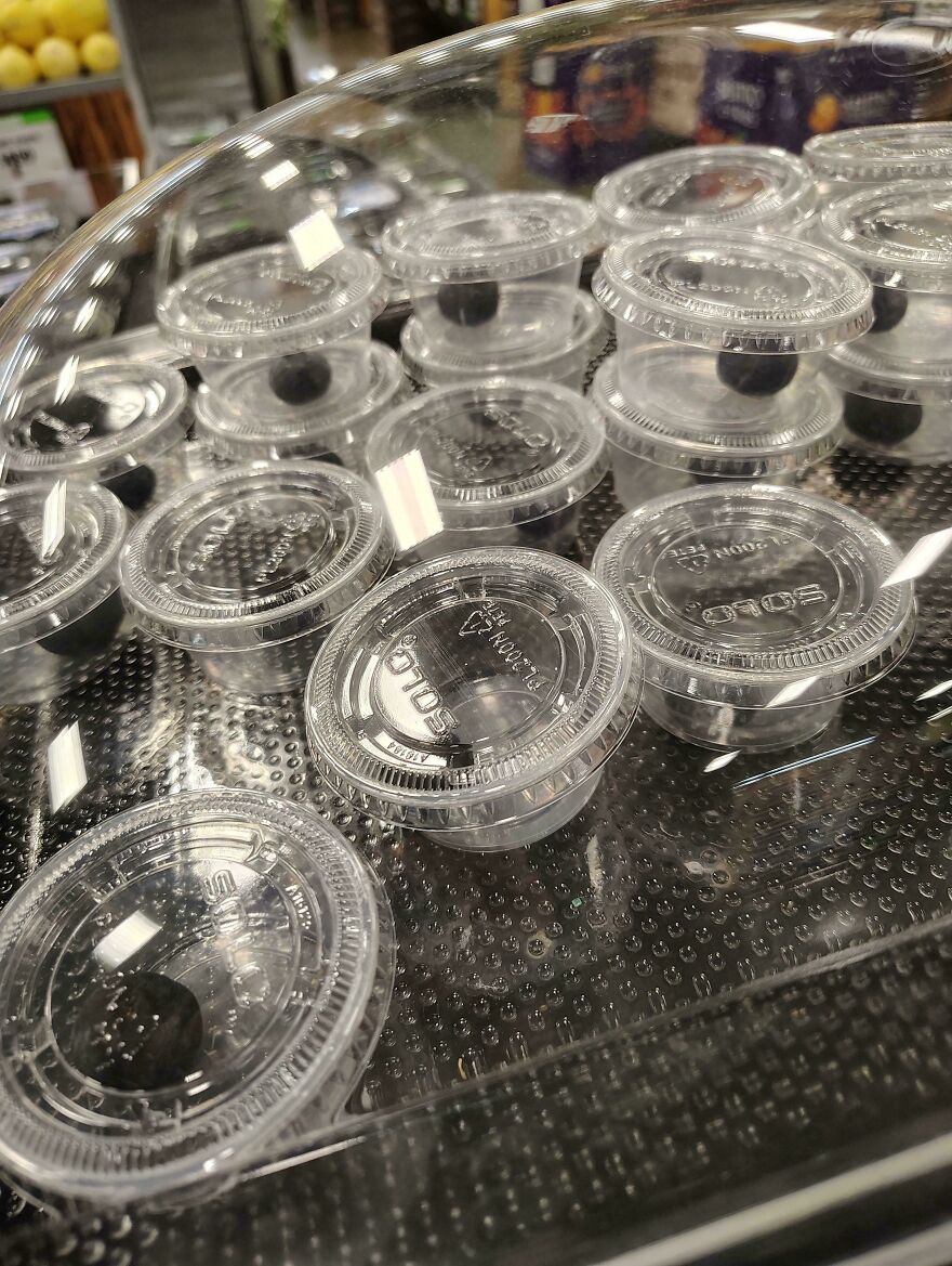 Plastic cups with a single blueberry, illustrating wasteful unnecessary packaging in a grocery store.