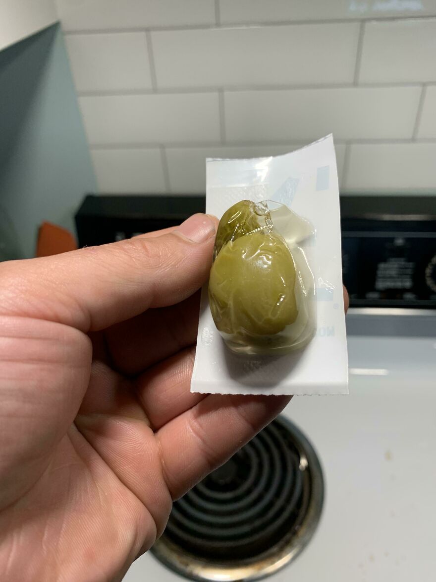 Hand holding an olive encased in unnecessary packaging.