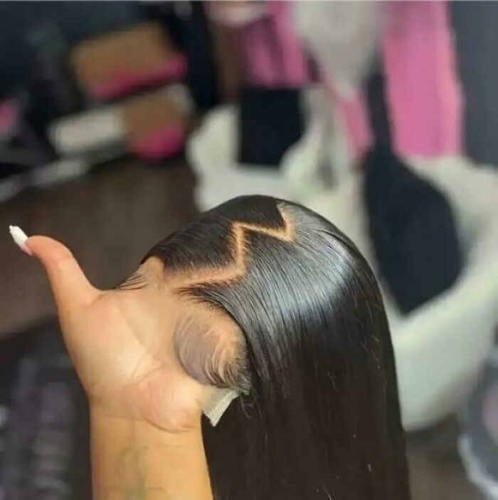 Confusing perspective showing a hand holding a wig styled with a zigzag pattern, creating an optical illusion.