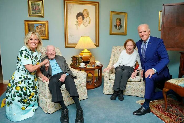 Confusing perspective photo of four people seated in a room with framed portraits on the walls.