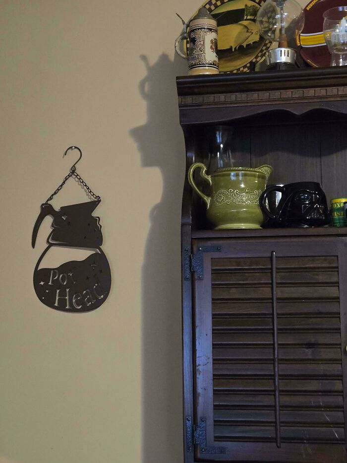 Confusing perspectives: shadow casts a profile of a person on the wall next to a shelf with various decorative items.