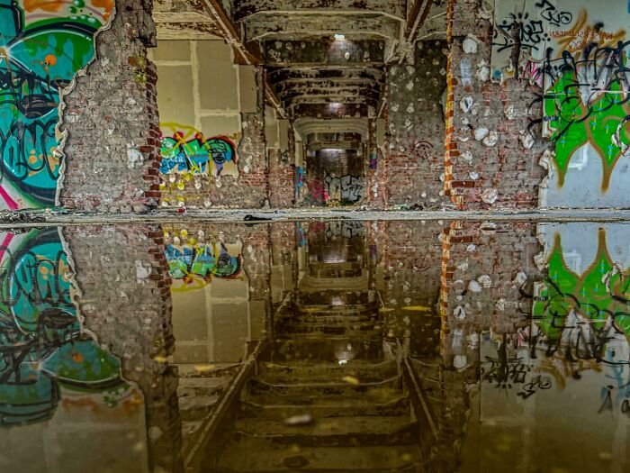 Graffiti-covered hallway reflecting in water, creating a confusing perspective.