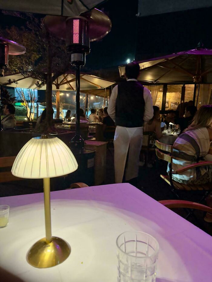 Confusing perspective: Lamp appears as man's head in a busy outdoor restaurant setting.