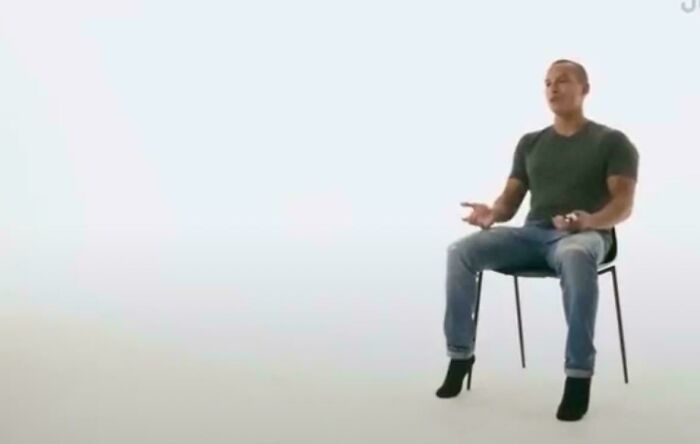 Man seated on chair appears to wear high heels, creating a confusing perspective.