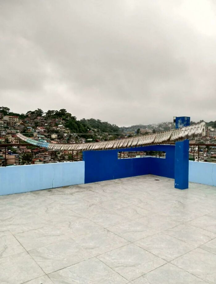 Confusing perspectives: rooftop with optical illusion of a bent roof, cloudy sky, and cityscape in the background.