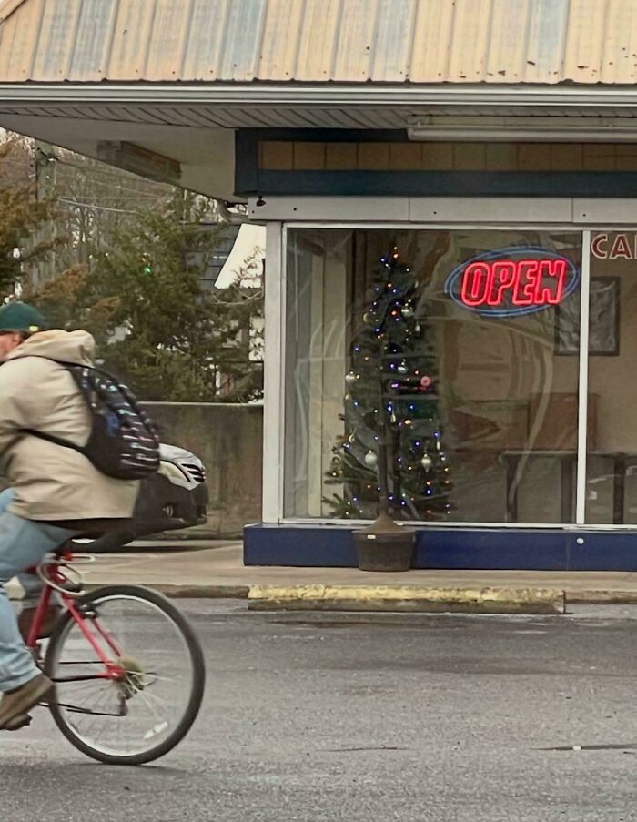 Confusing perspective with a cyclist appearing to ride through a Christmas tree inside a store with an "open" sign.