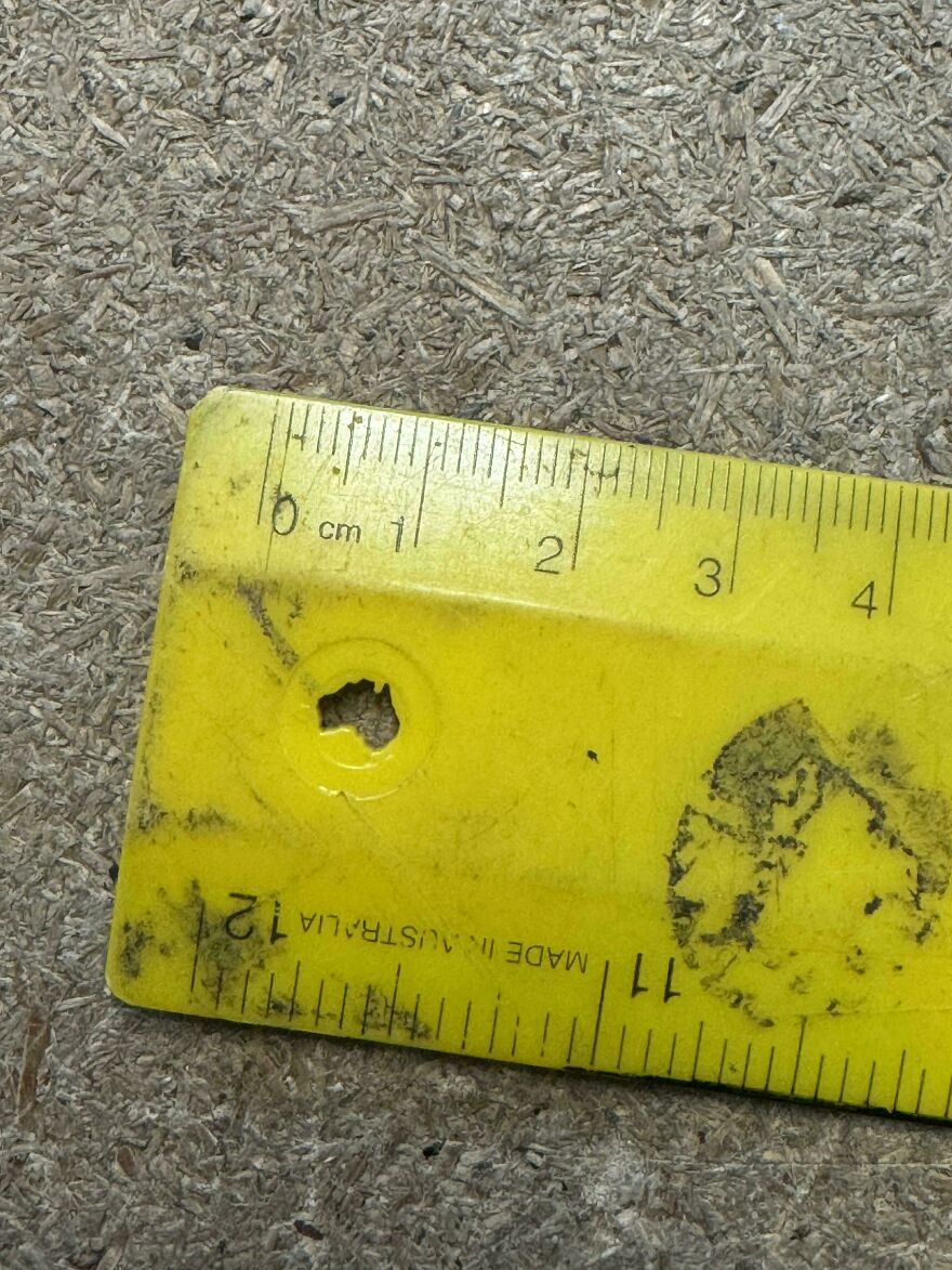 Yellow ruler with a hole resembling a bullet impact on a textured surface, illustrating "things look like other things."