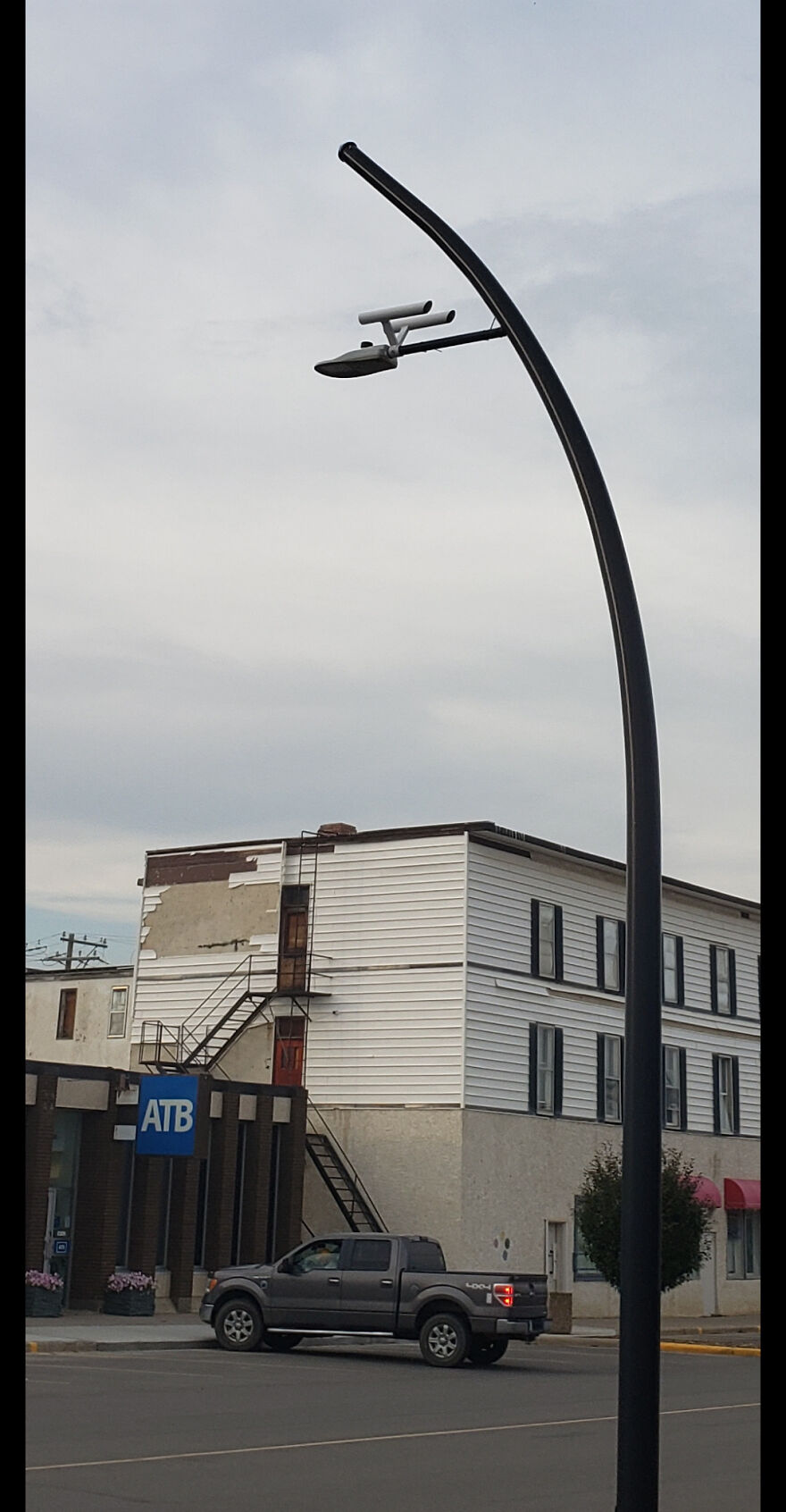 Streetlight shaped like an airplane, blending into an urban setting with buildings and a parked truck below.