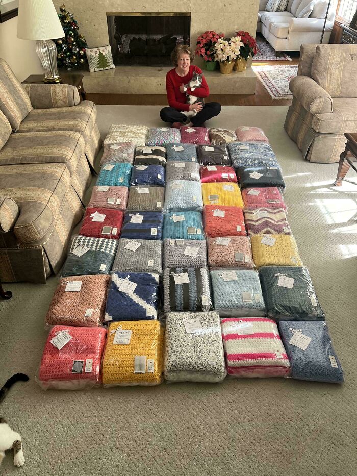 Person sitting with a pet behind a display of colorful crocheted blankets on the floor.