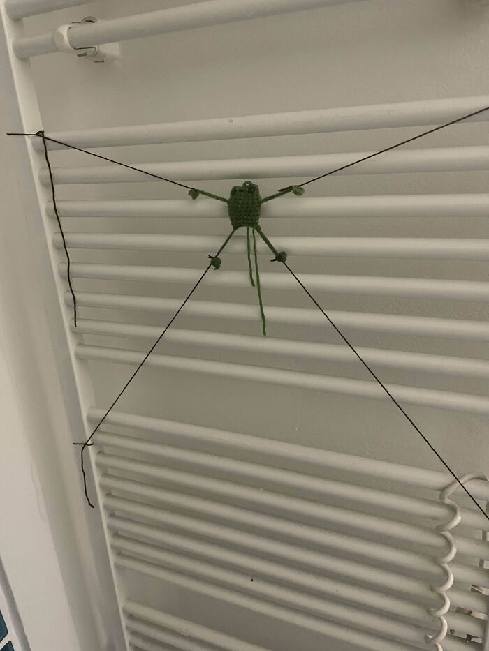 Crocheted green spider with string legs on a white radiator.