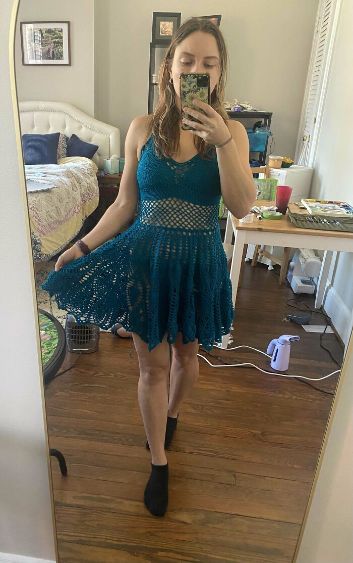 Person modeling a teal crocheted dress in front of a mirror.