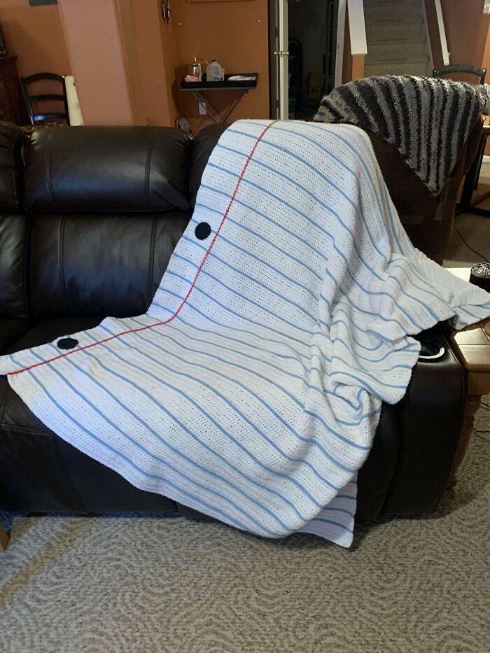 Crocheted blanket resembling a sheet of notebook paper draped over a dark leather couch.