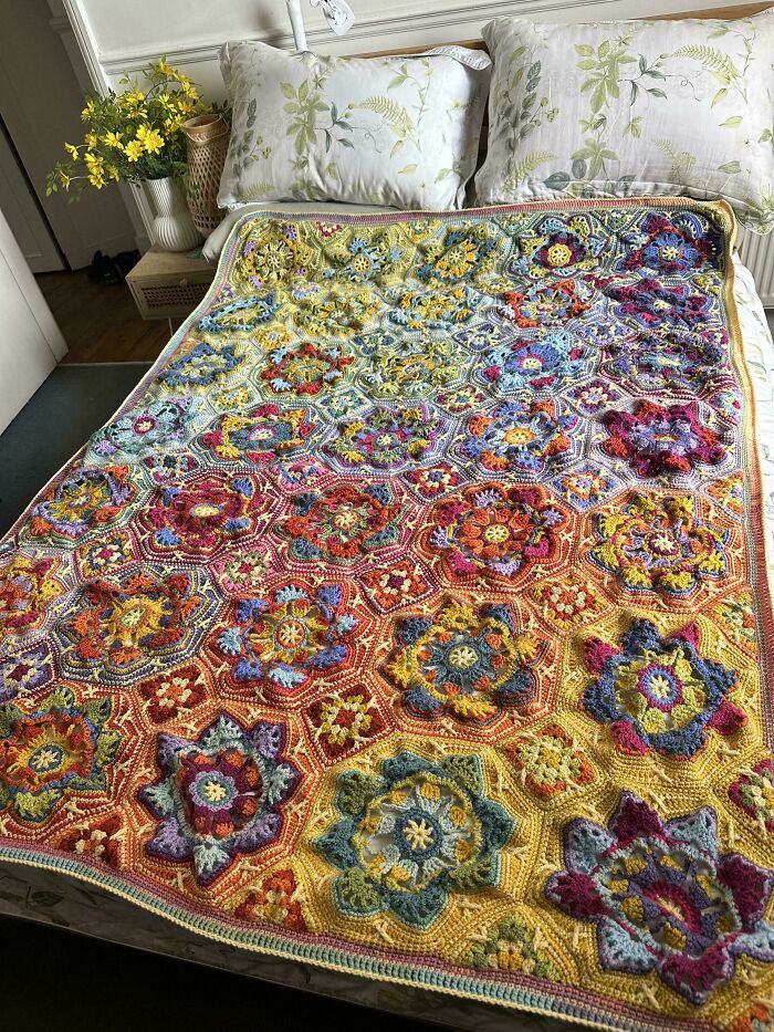 Colorful crocheted blanket with intricate floral patterns displayed on a bed.