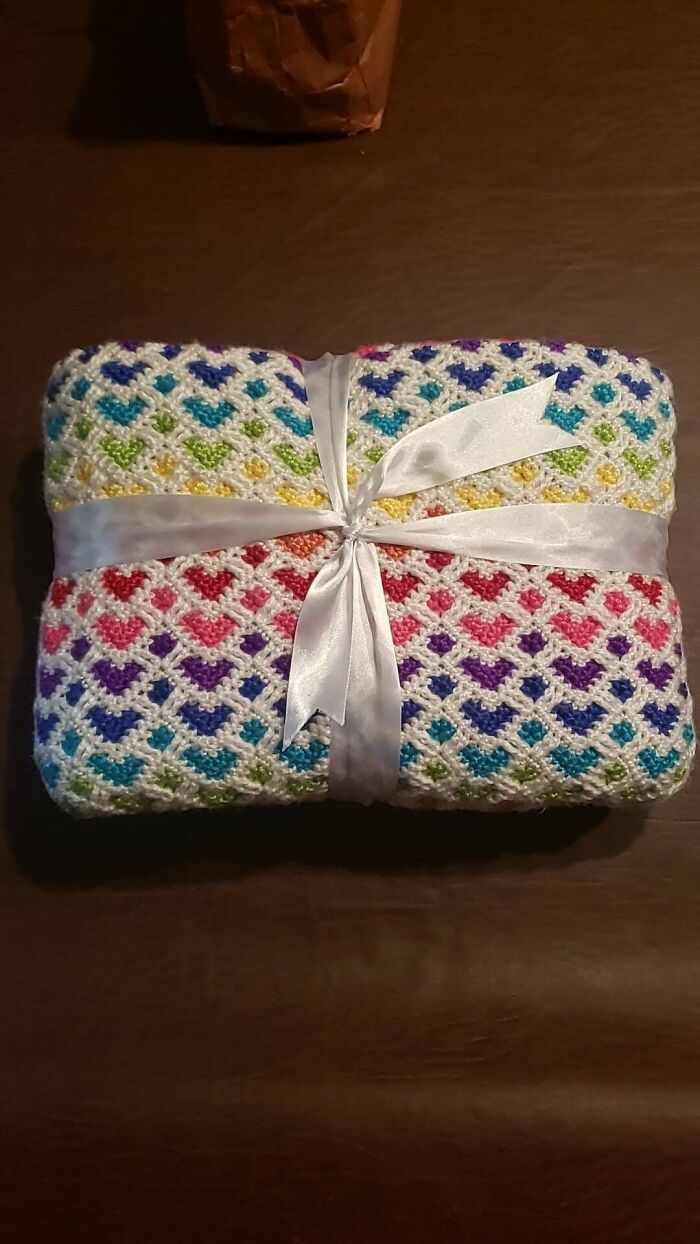 Colorful crocheted blanket with heart patterns, tied with a white ribbon on a brown surface.