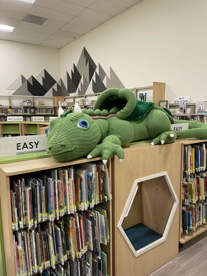 Crocheted green dragon displayed atop a library bookshelf.