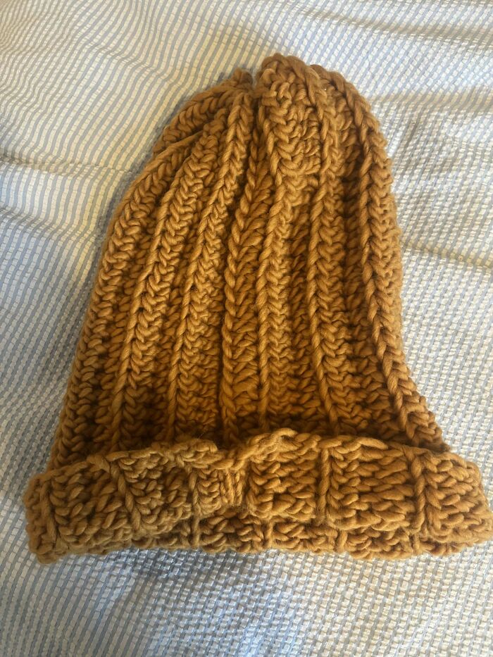 A crocheted beanie in chunky brown yarn displayed on a striped fabric background.