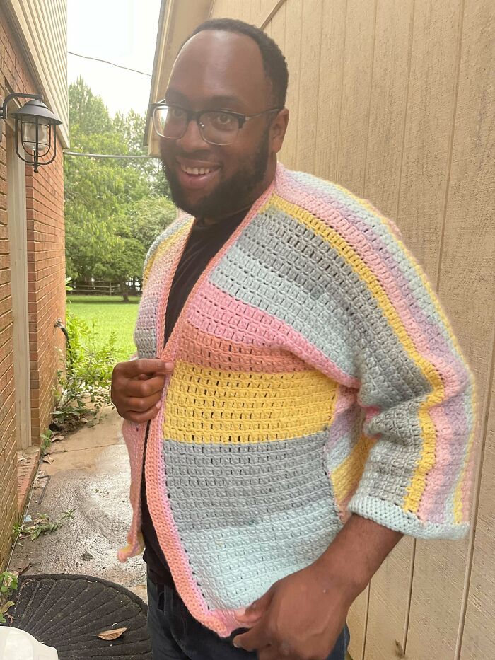 Person smiling in a colorful crocheted cardigan outdoors.