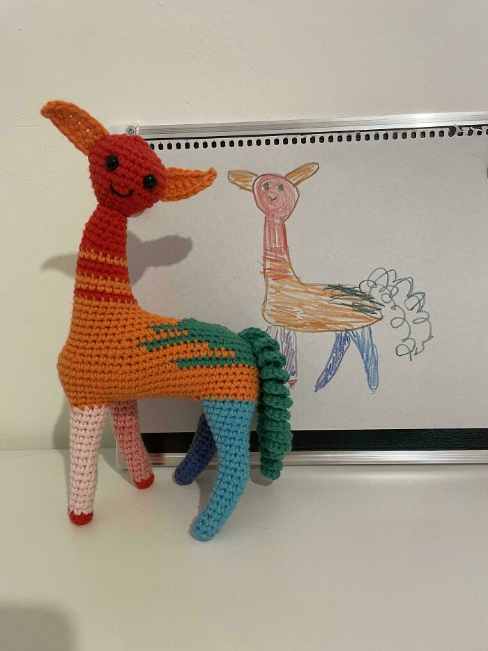 Colorful crocheted animal in front of a child's drawing, showcasing creativity and crochet craftsmanship.