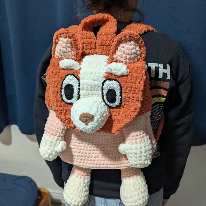 Crocheted animal backpack worn by a person, featuring a plush lion design with large eyes.