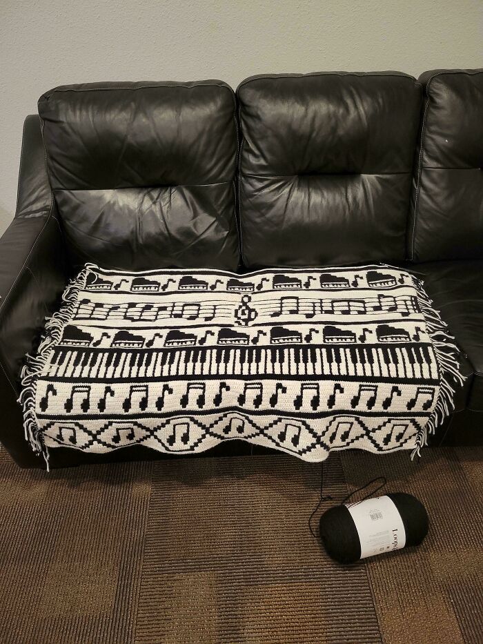 Crocheted blanket with musical notes and piano keys design on a black leather couch.