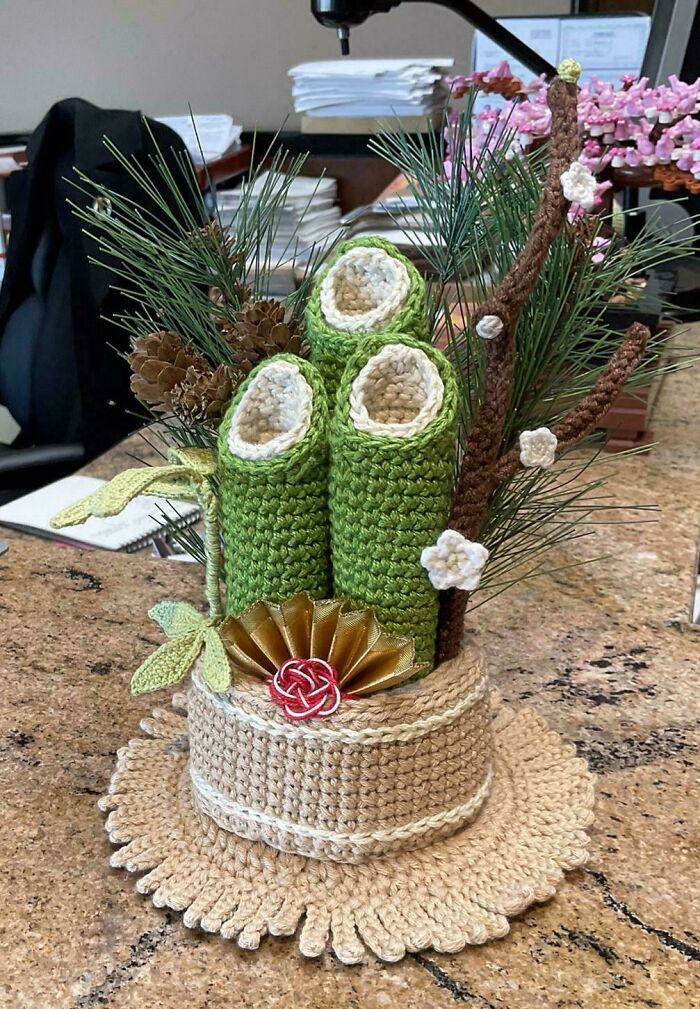 Crocheted decorative arrangement with green plants and flowers on a textured base.