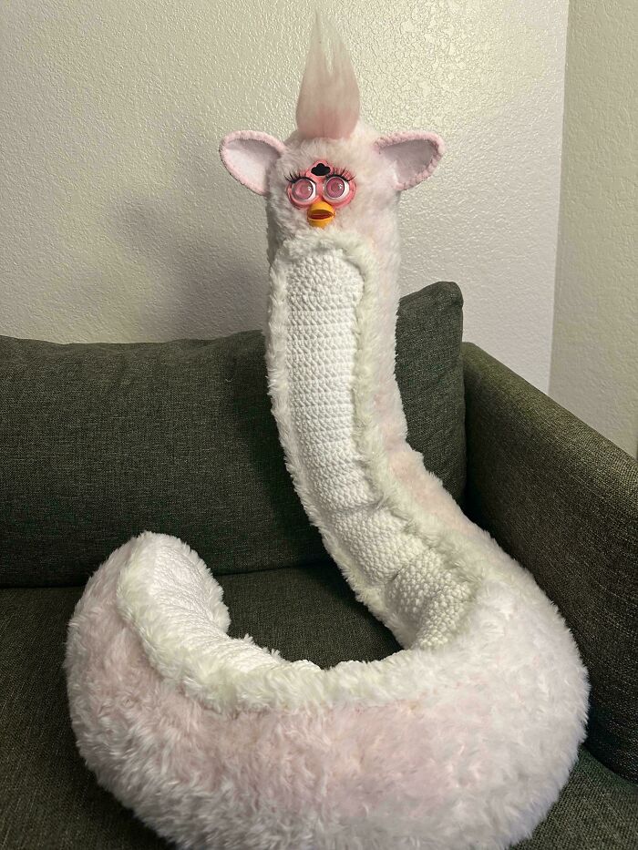 A crocheted creature with a long body and fluffy ears, sitting on a couch, showcasing incredible crochet artistry.