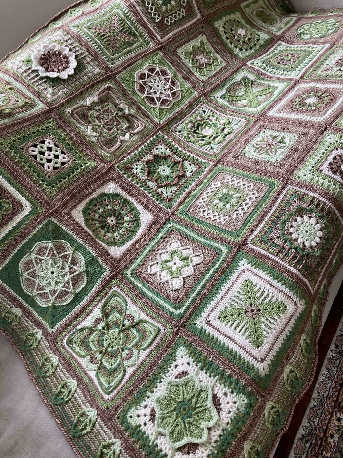 Crocheted blanket with intricate green and brown square patterns.