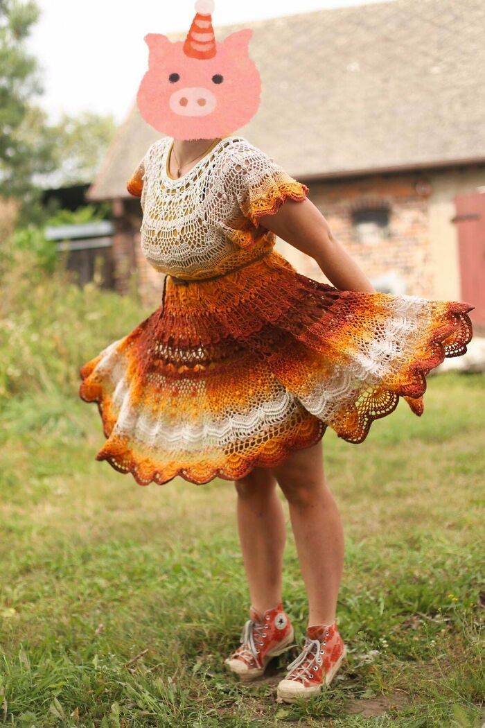 Person wearing a colorful crocheted dress with orange and brown hues, standing outside.