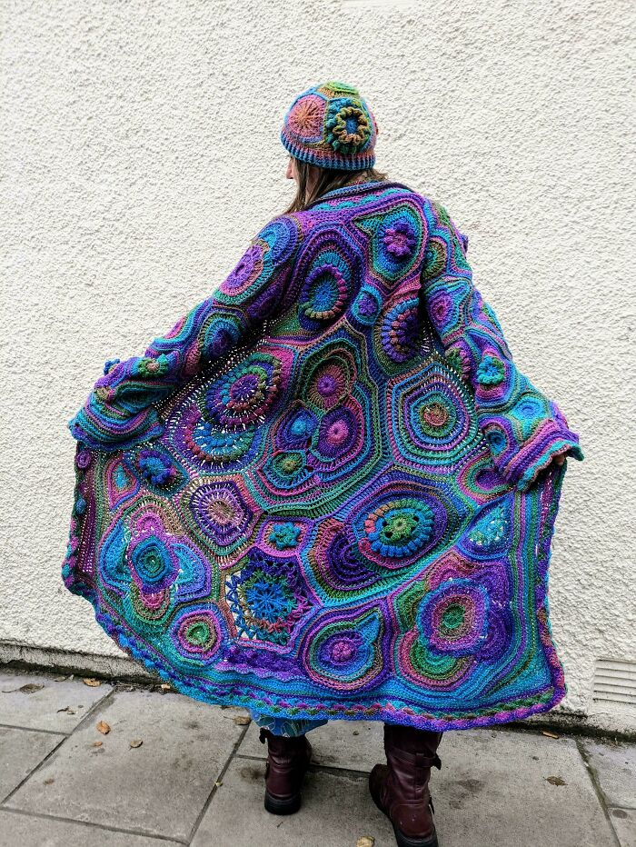 Person wearing colorful crocheted coat and hat with intricate patterns.