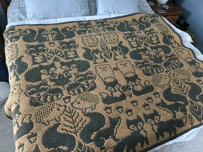 Intricate crocheted blanket with animal patterns displayed on a bed.