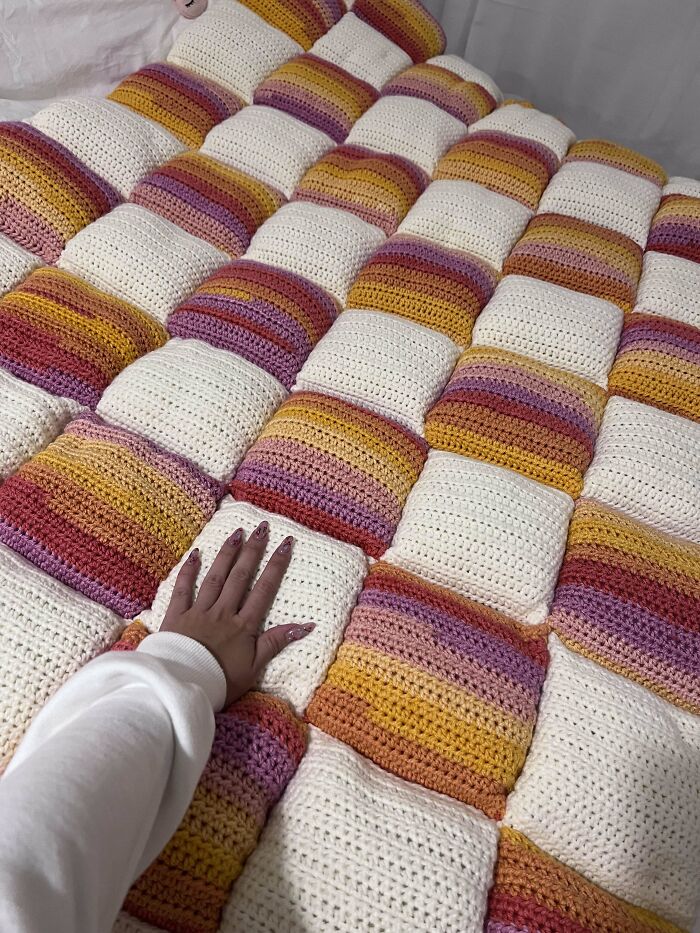 Hand touching a crocheted blanket with colorful striped and white squares.