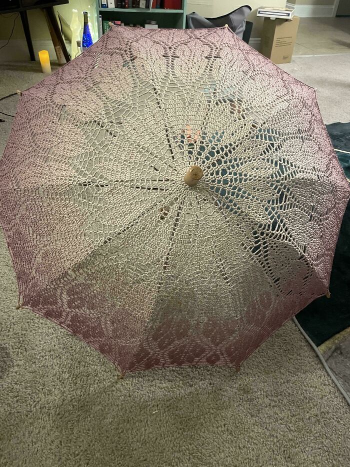 Crocheted parasol with intricate lace pattern on display indoors.